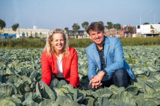 Foto van de laatste koolteelt op het perceel waar de nieuwe productielocatie komt. Op de foto zijn te zien Anouk Wissink, algemeen directeur Koninklijke Vezet en Marcel Jacobs, chief executive officer van Kramer Food Family. Op de achtergrond is de huidige productielocatie van Koninklijke Vezet te zien. - Beeld: Marloes Verweij